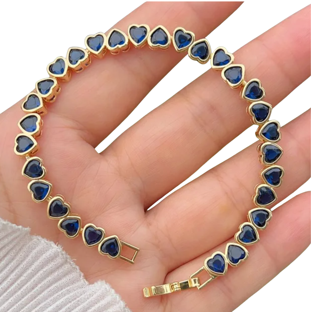 Gold bracelet with blue heart-shaped stones on a hand against a white background